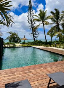 a swimming pool with a wooden deck and palm trees at Tropical beachfront apartment in Belle Mare