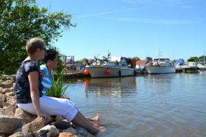 dos personas sentadas en rocas cerca del agua con barcos en Ferienwohnung Jaeschke_ 25669 en Weener