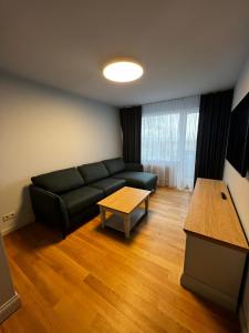 Una sala de estar con un sofá negro y una mesa. en Sunrise Lauku Apartments, en Liepāja