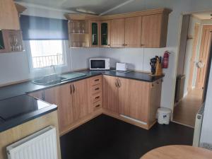 a kitchen with wooden cabinets and a microwave at S295 3 BED DELUXE PET FRIENDLY CARAVAN in Chapel Saint Leonards