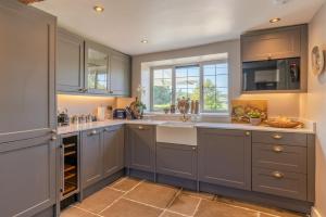 a kitchen with gray cabinets and a sink and a window at Broughwood Cottage Snowshill in Broadway