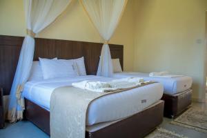 2 Betten in einem Schlafzimmer mit weißer Bettwäsche und Vorhängen in der Unterkunft Lake Bogoria Spa Kabarak in Nakuru
