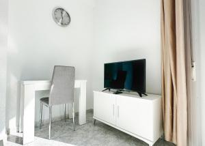 einen Fernseher auf einem weißen Schrank mit Stuhl und Uhr in der Unterkunft Skol 131 - Studio at Skol Building in Marbella centre with sea views. in Marbella