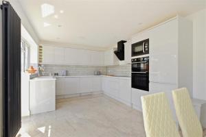 a white kitchen with white cabinets and black appliances at Stunning family home, walking distance to Herne Bay Beach! in Kent