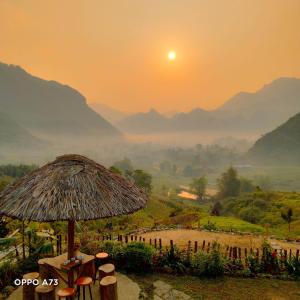 a sunrise with a straw umbrella and mountains in the background at Du Gia Panorama in Làng Cac