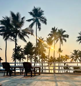 Una mesa y sillas en la playa con palmeras. en Sunset Ville Beach Resort, en Varkala