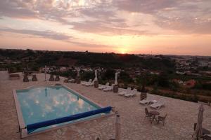 a swimming pool with chairs and a sunset in the background at The Olive Hill Guesthouse in Batalha