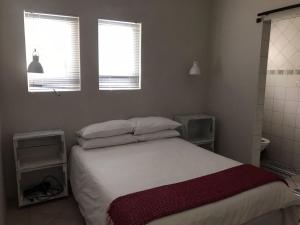 a bedroom with a bed with white sheets and two windows at A Touch of Red in Oudtshoorn