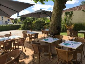 a patio with tables and chairs and an umbrella at Hôtel La Cote d'Argent in Seignosse