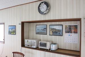 a clock on a wall above a counter with a microwave at Minshuku Katsuya in Shirahama