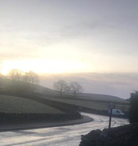 uma estrada sinuosa com o pôr do sol no horizonte em George & Dragon em Aysgarth