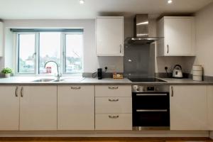een keuken met witte kasten, een wastafel en een fornuis bij James Charles Apartments in Milton Keynes