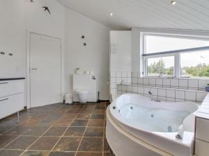 een witte badkamer met een bad en een raam bij Holiday Home Senni - 1-1km from the sea in NW Jutland by Interhome in Løkken