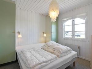 Un dormitorio con una cama con sábanas blancas y una lámpara de araña. en Holiday Home Adelita - 100m from the sea in NW Jutland by Interhome, en Løkken