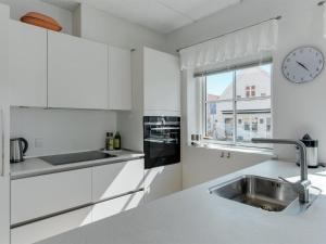uma cozinha branca com um lavatório e um relógio na parede em Apartment Cornel - 400m from the sea in NW Jutland by Interhome em Hjørring