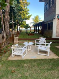 a group of white chairs and a table in the grass at Vila Japaraiso-Casa Amarela Próxima ao mar in Japaratinga