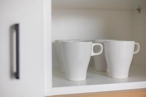two white coffee cups sitting on a shelf at Aparthotel Esencja Warszawy Nowy Świat in Warsaw