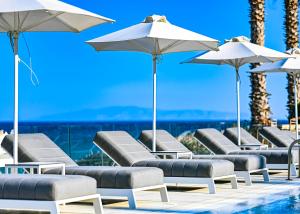 a row of lounge chairs and umbrellas next to a swimming pool at Saint George Hotel in Chrissi Akti