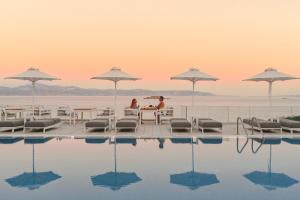 a couple sitting at a table next to a swimming pool at Saint George Hotel in Chrissi Akti
