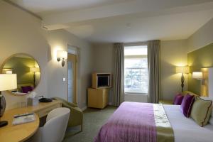 a hotel room with a bed and a desk and a mirror at The Lensbury Resort in Richmond upon Thames