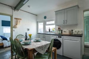una cocina con mesa y sillas y una cocina con armarios blancos. en Cobweb Cottage en Waenfawr