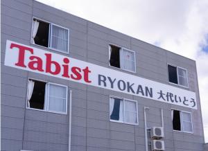 a building with a sign on the side of it at Tabist Oshiro Ito Tagajo in Tagajo