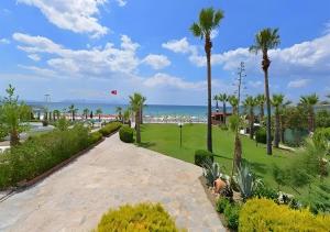een wandelpad door een park met palmbomen en het strand bij Sentinus Beach Hotel in Kuşadası