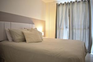 a white bed with white pillows and a window at Mediterrâneo 507 - Todo Equipado, Ar Condicionado, Churrasqueira na Varanda, Internet Fibra 600MB, Estacionamento Grátis in Cabo Frio
