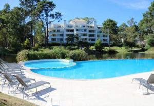 a large swimming pool with lounge chairs and a building at Departamento con jardin en Green Park, Punta del Este in Punta del Este