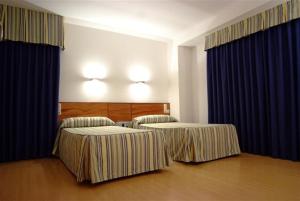 two beds in a hotel room with blue curtains at Colón Tuy in Tui