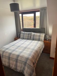 a bedroom with a bed with a plaid blanket and a window at Almondbank Self Catering Apartment in Skeabost