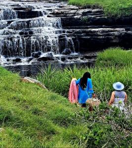 two people sitting in the grass near a waterfall at Wild Coast Grosvenor Holiday Home in Lusikisiki