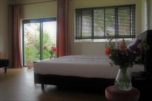 Un dormitorio con una cama y una ventana con flores en un jarrón en Bed & Breakfast Bij de Wilg en Laren