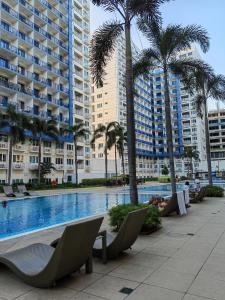 een zwembad met stoelen, palmbomen en gebouwen bij Apartment by Casarenta at Sea Residences in Manilla
