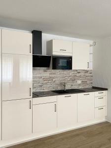 Una cocina blanca con armarios blancos y una pared de piedra. en Sehr zentral, geräumiges, helles Studio-Apartment en Colonia