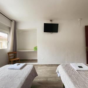 Habitación con 2 camas y TV en la pared. en HOSTAL MONREAL, en San Juan de Alicante