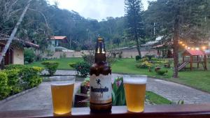 a bottle of beer sitting on a table with two glasses at Sitio do Imbuí em Teresópolis in Teresópolis