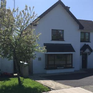 Una casa blanca con un árbol delante. en Summer Cottage in Kinsale en Kinsale