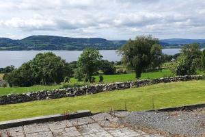 a field with a stone wall and a lake at Cosy self contained cottage with stunning views in Killaloe