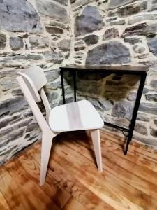 a white chair and a table in front of a stone wall at El Puente Peregrino in Trabadelo