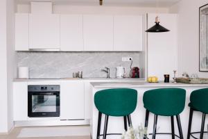 a kitchen with white cabinets and green bar stools at Design Apartman - Free parking in Szeged