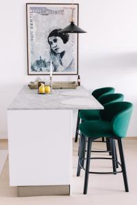 a kitchen with a white counter and green chairs at Design Apartman - Free parking in Szeged