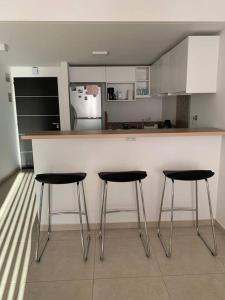 a kitchen with three bar stools in front of a counter at Hermoso depto en excelente ubicacion in Puerto Madryn