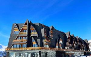 a building with a black roof with mountains in the background at Marshall Gudauri Apartment SkiCasa in Gudauri