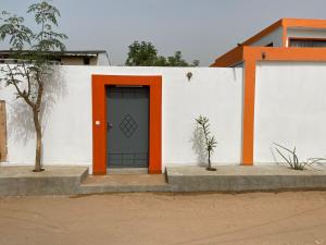 ein weißes Gebäude mit einer orangefarbenen Tür drauf in der Unterkunft Studio neuf independant dans villa in Ouoran