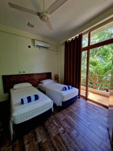 2 Betten in einem Zimmer mit einem großen Fenster in der Unterkunft Finolhu Beach Guest House in Felidhu-Atoll