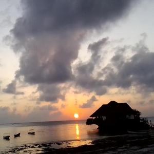a sunset on a beach with boats in the water at Bibi Mrembo Guesthouse in Pingwe