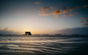 a sunset over the ocean with a building in the distance at Seaside 43 in Sankt Peter-Ording