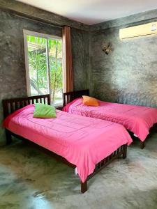 two beds in a room with pink sheets and a window at Bansuanrimnam Pakchong Resort in Pak Chong