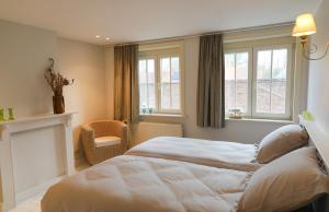 a bedroom with a bed and a chair and windows at Maison Rose in Ypres